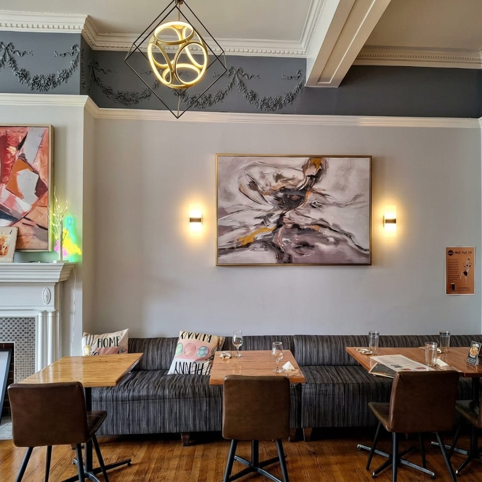 Restaurant interior with modern art, a long striped booth, wooden tables, and brown chairs.