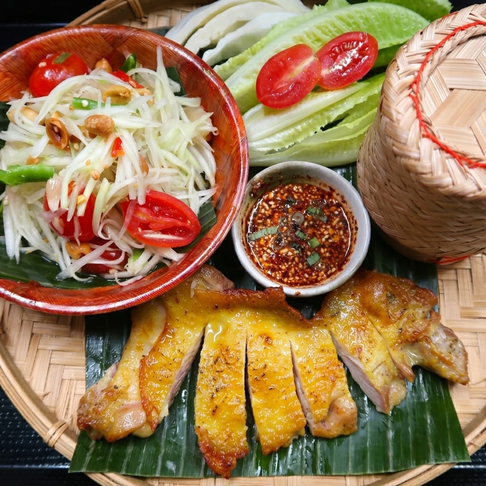 Grilled chicken, papaya salad, dipping sauce, lettuce, tomatoes, and sticky rice on a bamboo tray.