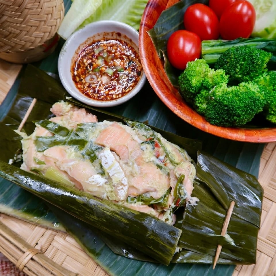 Steamed salmon with vegetables and dipping sauce, served on banana leaves.